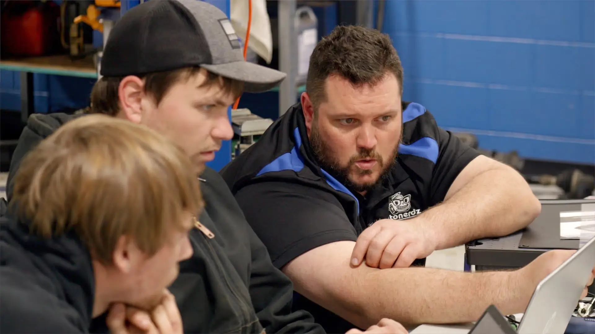 Three individuals in a workshop setting focusing on a technical task with a laptop, possibly involved in an automotive PicoScope training session.