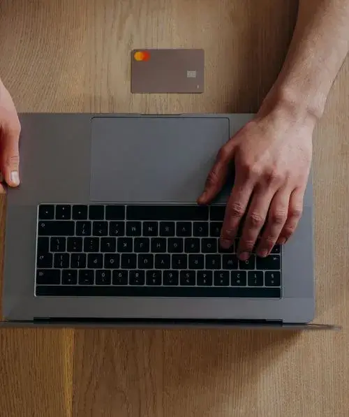 A person using a laptop with a credit card nearby, suggesting online shopping or e-commerce activity.