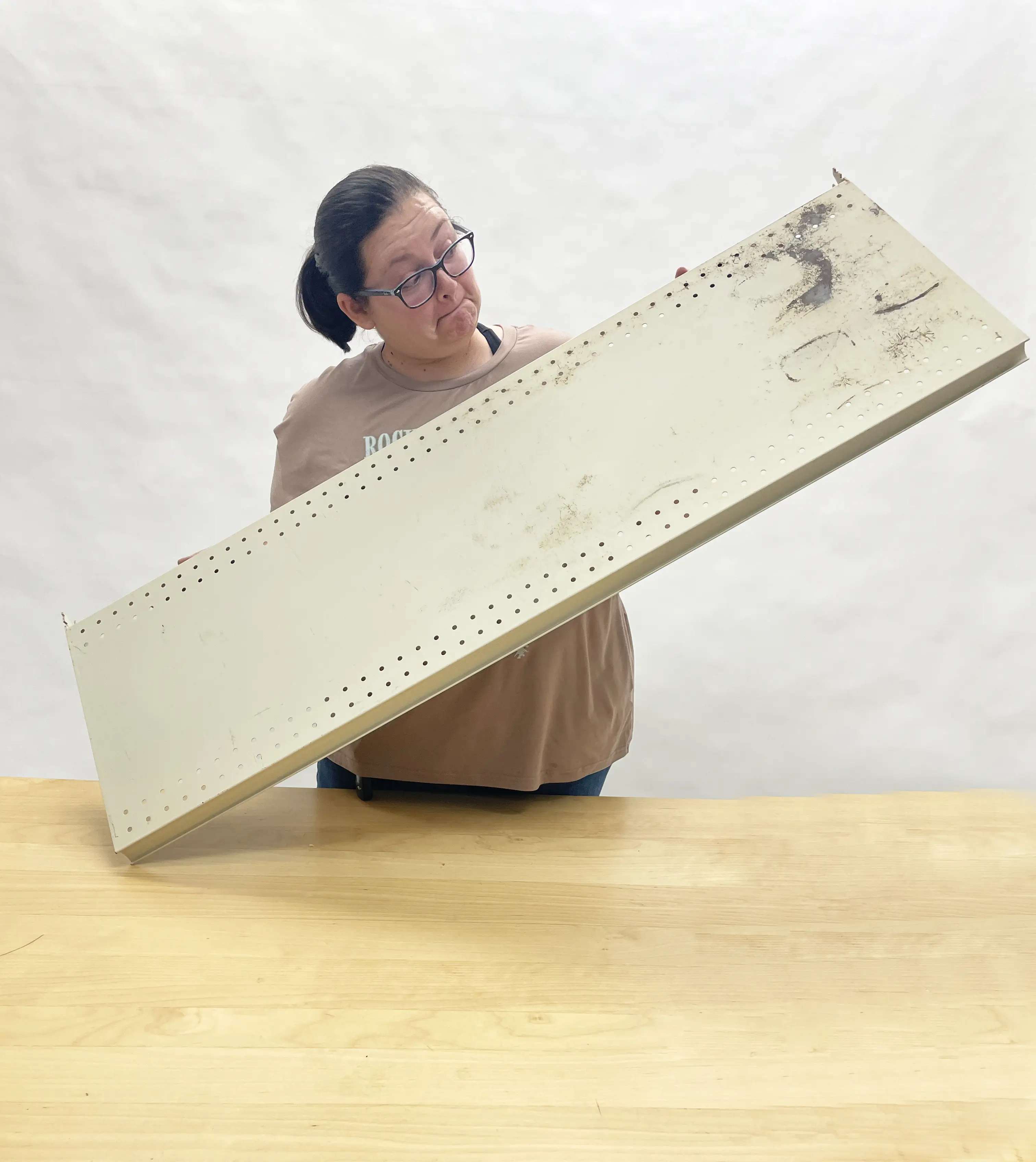 A person holding a worn retail shelving unit over a wooden table, inspecting it closely.